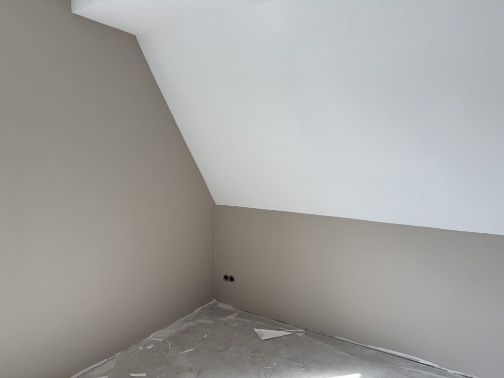 Zolderkamer in een nieuwbouwwoning met een schuine wand, afgewerkt in een lichte grijstint en wit