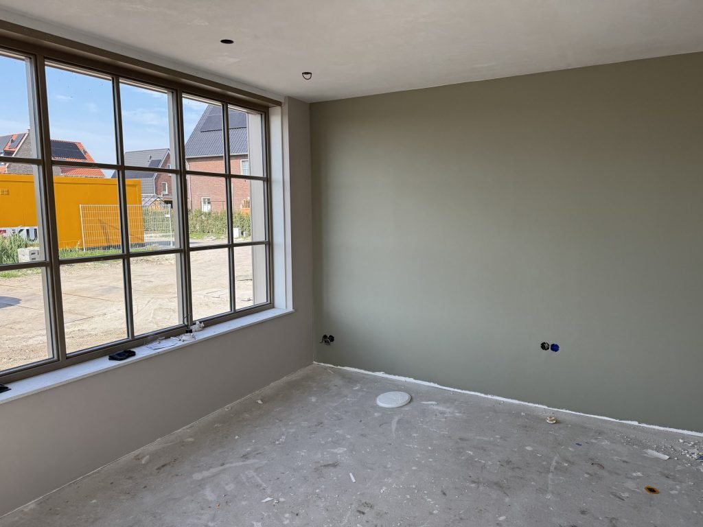 Nieuwbouwkamer met een egaal afgewerkte wand in een grijsgroene tint en een groot raam